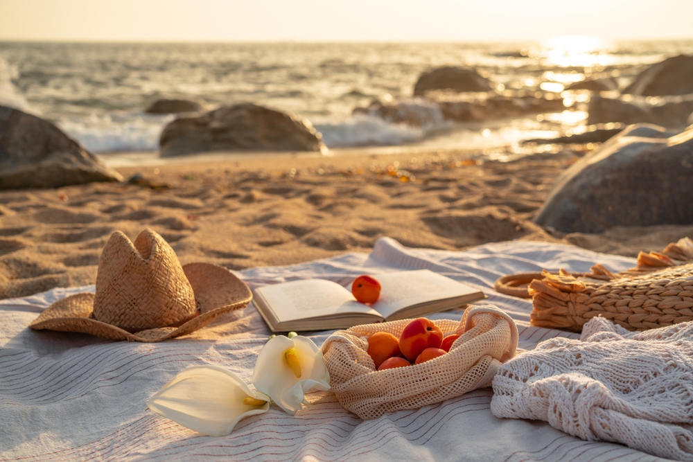 Sunset beach picnic scene with apricots, book, and straw hat on a blanket by the ocean