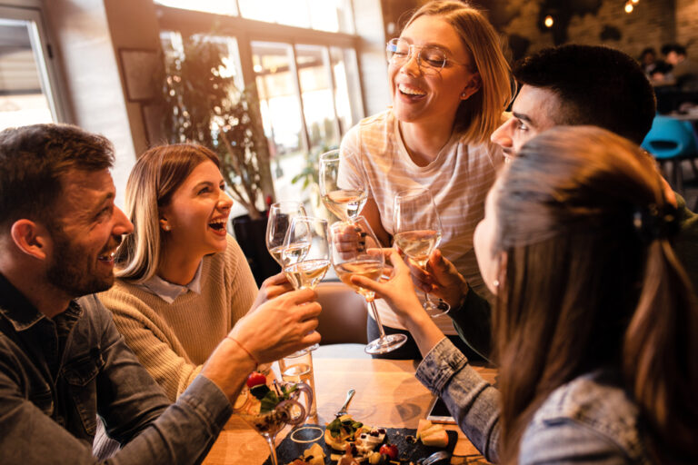 Group of young friends having fun in restaurant, talking and laughing while dining at table.