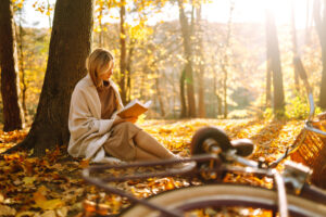 Beautiful young woman sitting on a fallen autumn leaves in a park, reading a book.