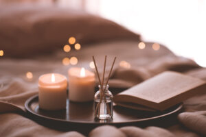 Bamboo sticks in bottle with scented candles and open book on wooden tray in bed closeup. Home aroma.