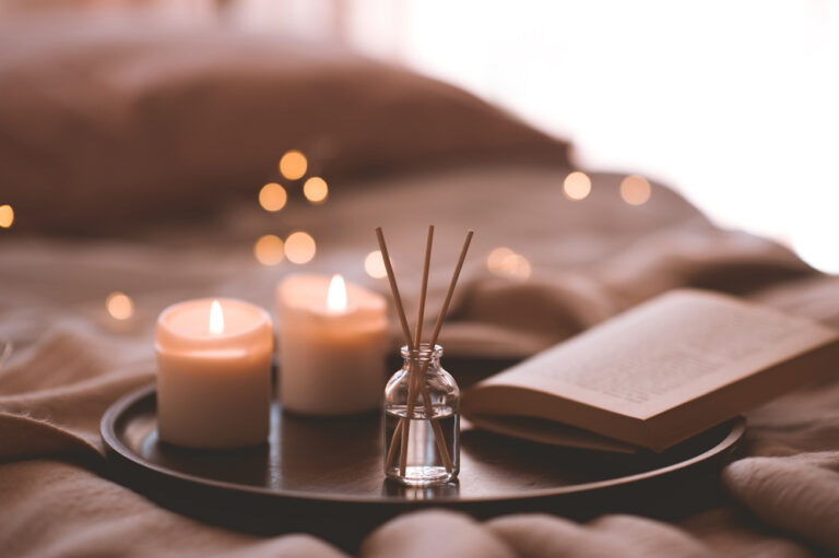 Bamboo sticks in bottle with scented candles and open book on wooden tray in bed closeup. Home aroma.