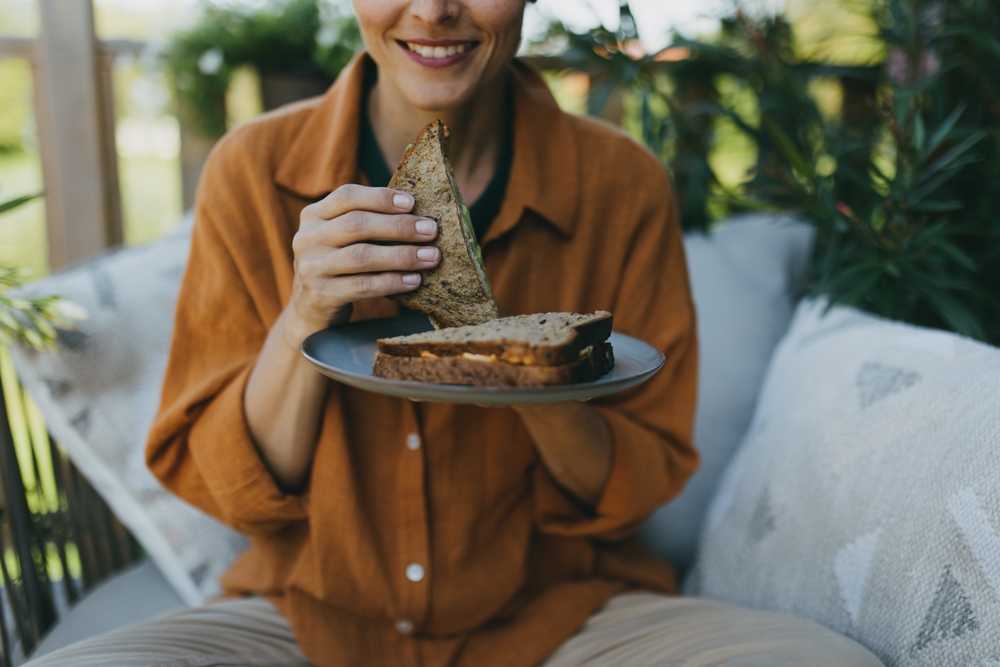 Beautiful woman relaxing in the garden, eating sandwich. Mother having moment to herself while her child is sleeping, eating lunch or dinner in peace.