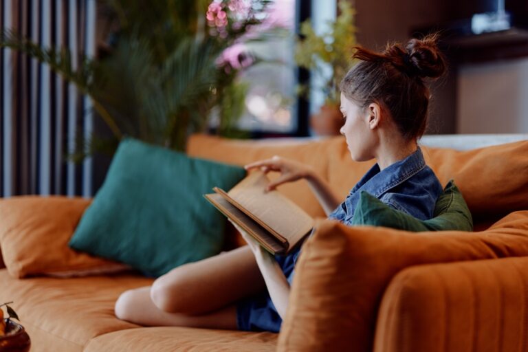 Cozy evening at home woman relaxing on orange couch with book and cup of coffee, warm and inviting atmosphere