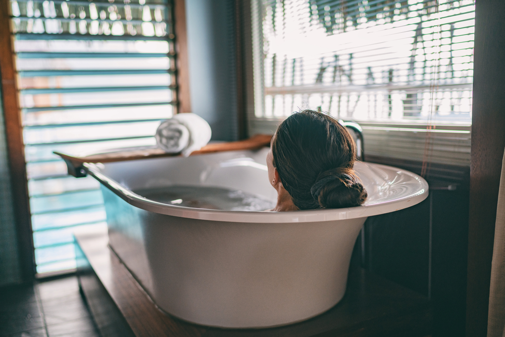 Bath taking woman relaxing in bathtub of hotel room at luxury overwater bungalow resort in Bora Bora, Tahiti.