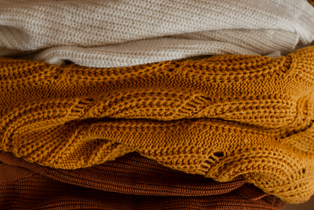 Close up of texture of differnets knitted sweaters. Autumn colorful palette of warm sweatshirts on table. Concept of winter  autumn clothes.
