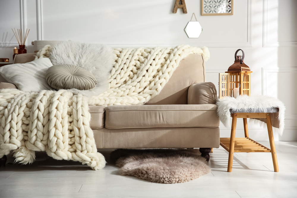 Cozy living room interior with beige sofa, knitted blanket and cushions