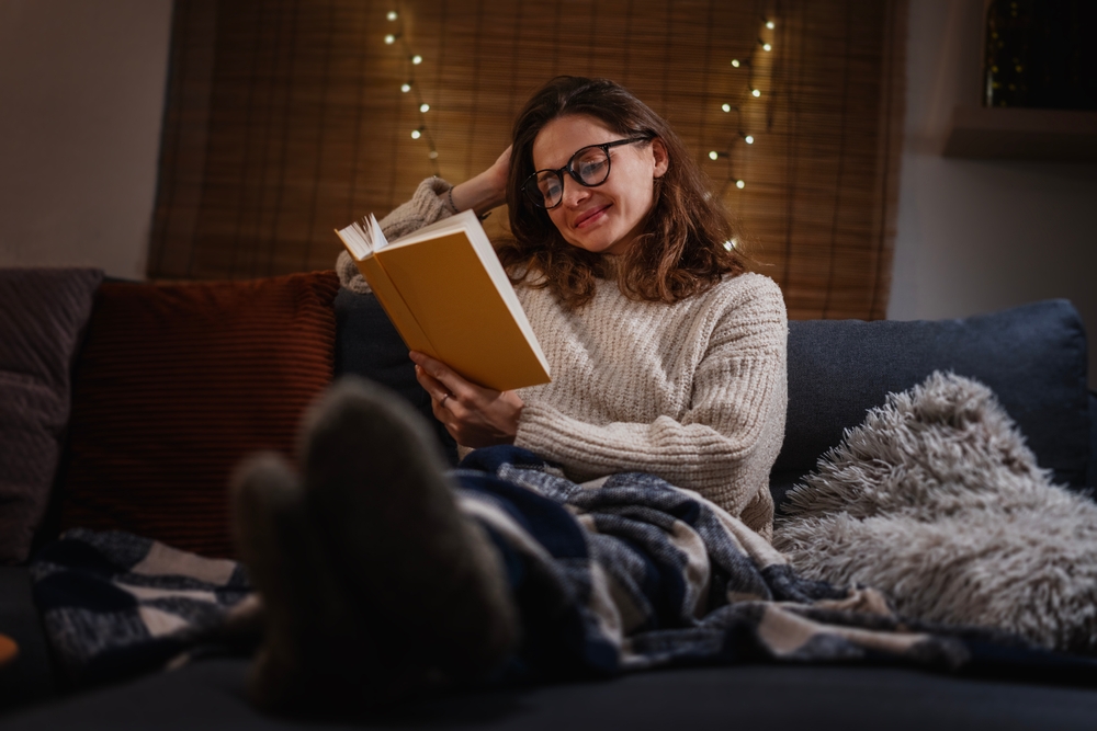 Portrait of smiling woman reading a book on couch at home in the evening
